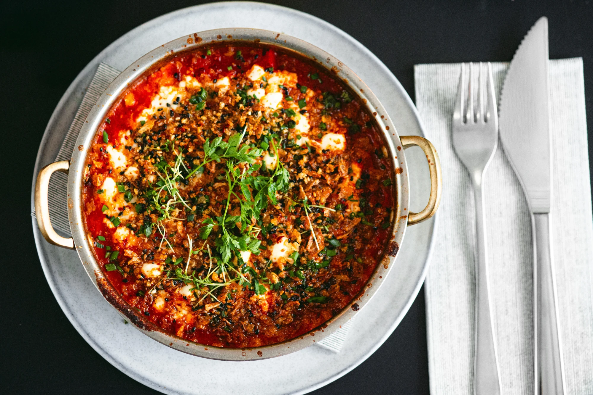 Shakshuka von oben in der Pfanne, mit Feta und frischen Kräutern