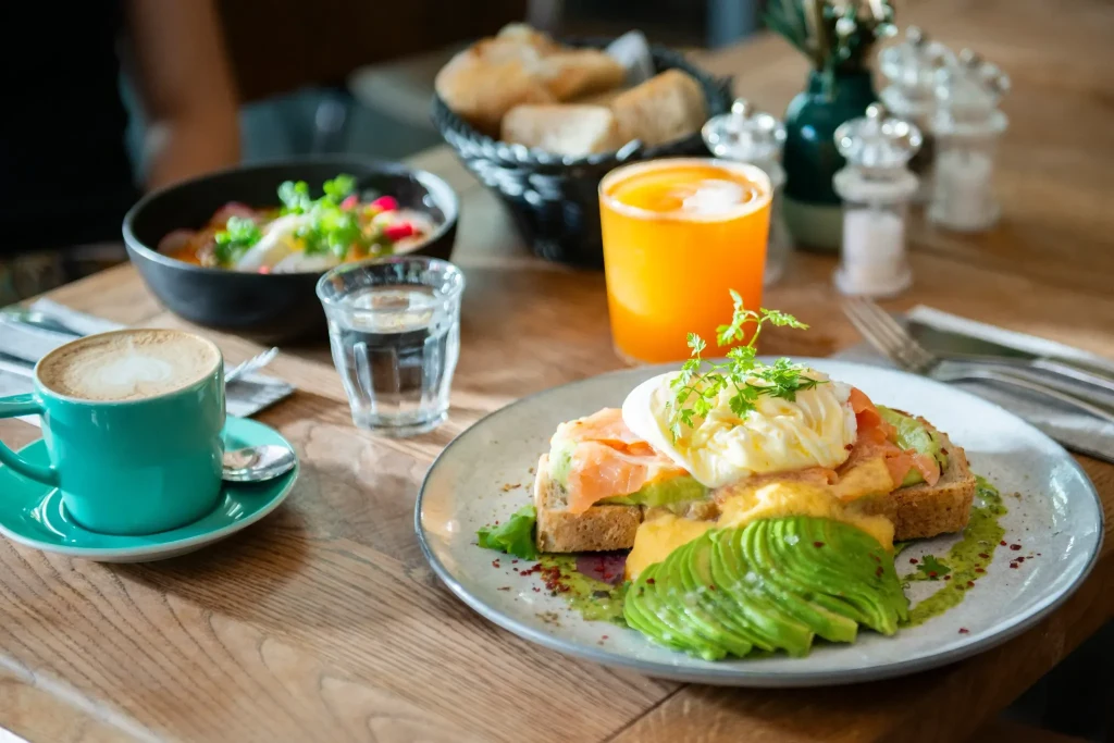 Avocado-Brot mit Salat, Orangensaft und Brotkorb auf dem Holztisch